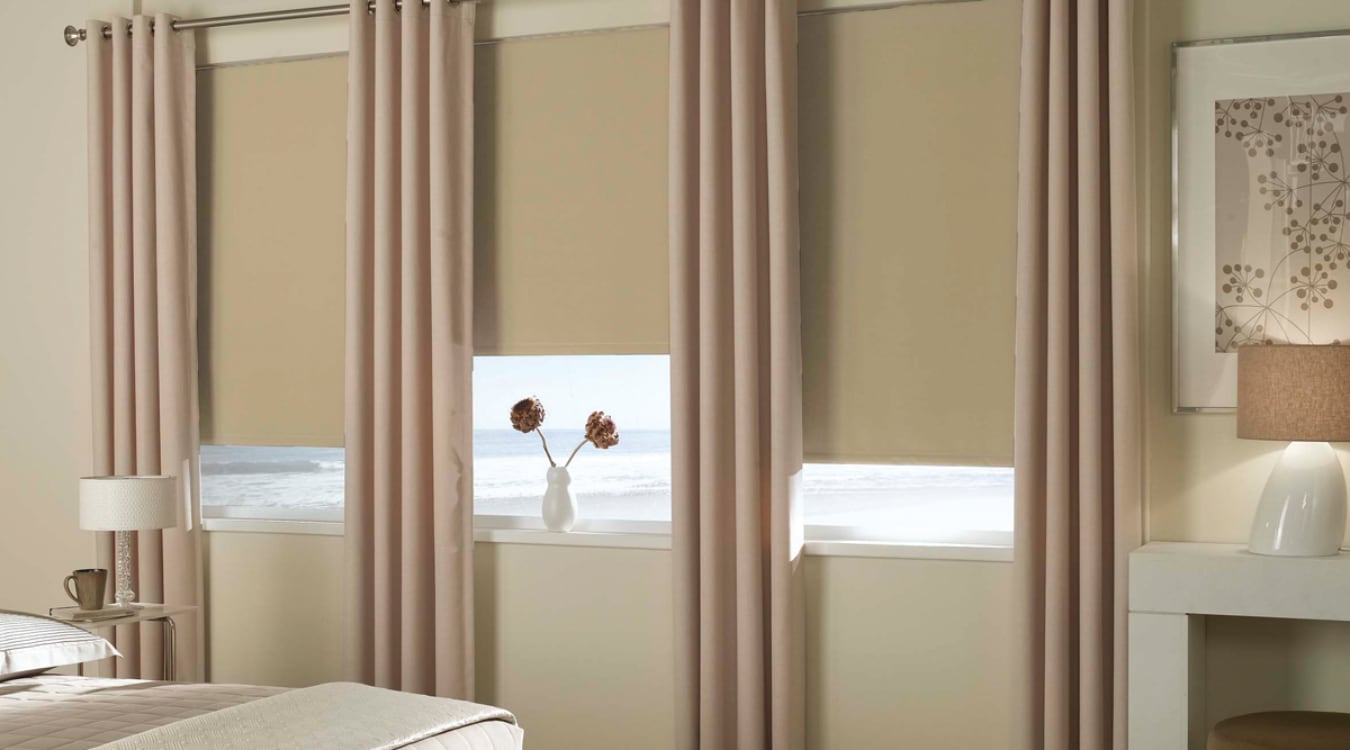 Layering shades with curtains is a quick way to reduce the amount of light coming into a room. Blackout roller shades layered with curtain